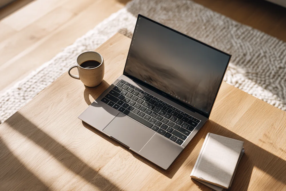 A laptop and coffee on a desk in morning light